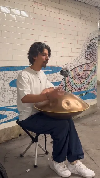 Gordey playing handpan in a mosaic-tiled NYC subway passage