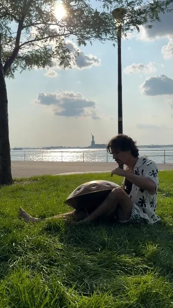 Gordey playing handpan on the grass by the water, Statue of Liberty in the distance